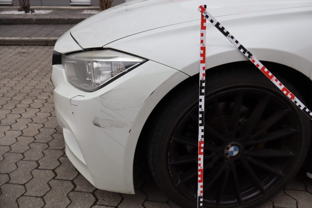 Kfz-Gutachter Fürth – Frontschaden an einem weißen BMW mit Maßstab zur Schadensdokumentation